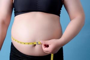 Overweight women are measuring Terry's belly fat using a tape measure and isolating the background on a blue background. photo