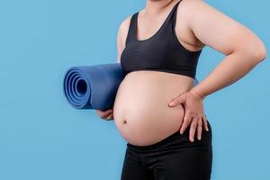 mujer gorda sosteniendo estera de yoga en el estudio. sobre un fondo azul. fondo aislado. foto