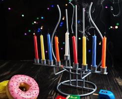 Jewish holiday Hanukkah background. Traditional dish is sweet donuts. Hanukkah table setting candlestick with candles and spinning tops on black background. Lighting Chanukah candles. Copy space photo