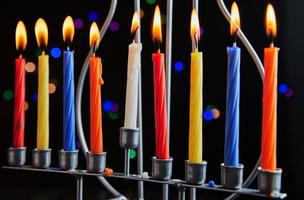 Jewish holiday Hanukkah background. A traditional dish is sweet donuts. Hanukkah table setting candlestick with candles and spinning tops on black background. Lighting Chanukah candles. Copy space photo