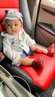 A child sits in a red black car looking at the driver's face photo