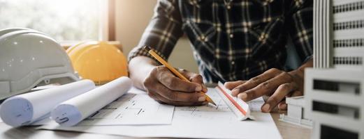 Image of engineer drawing a blue print design building or house, An engineer workplace with blueprints, pencil, protractor and safety helmet, Industry concept photo