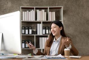 Young woman working on a laptop in the office. Asian businesswoman sitting at her workplace in the office. Beautiful Freelancer Woman working online at her home. photo