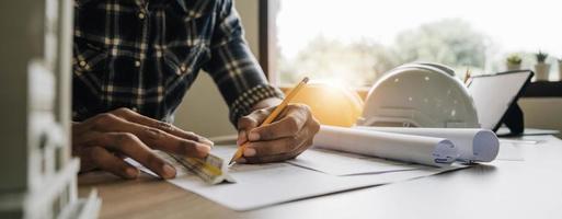 Image of engineer drawing a blue print design building or house, An engineer workplace with blueprints, pencil, protractor and safety helmet, Industry concept photo