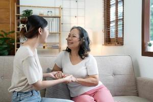 Happy adult granddaughter and senior grandmother having fun enjoying talk sit on sofa in modern living room, smiling old mother hugging young grown daughter bonding chatting relaxing at home together photo