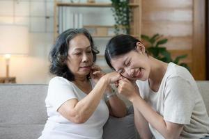 Happy adult granddaughter and senior grandmother having fun enjoying talk sit on sofa in modern living room, smiling old mother hugging young grown daughter bonding chatting relaxing at home together photo