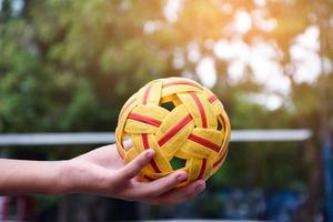 joven jugador de sepak takraw masculino del sudeste asiático usando su mano derecha para sostener la pelota antes de enviar a otro jugador a patear, sepak takraw al aire libre jugando después de la escuela, enfoque suave y selectivo en la pelota. foto