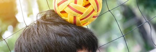 Young southeast asian male sepak takraw player using his right hand  to hold ball on his head, outdoor sepak takraw playing after school, soft and selective focus on ball. photo