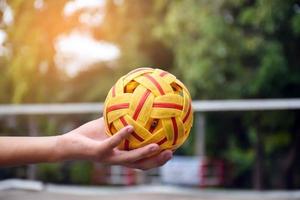 joven jugador de sepak takraw masculino del sudeste asiático usando su mano derecha para sostener la pelota antes de enviar a otro jugador a patear, sepak takraw al aire libre jugando después de la escuela, enfoque suave y selectivo en la pelota. foto