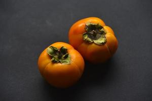 frutos de caqui naranja sobre un fondo negro. primer plano de frutos de caqui maduros y jugosos. foto