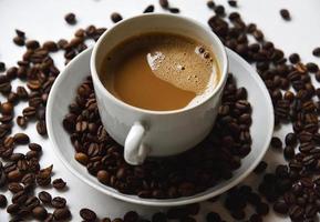 White porcelain cup with coffee and coffee beans on a white background. Tea pair with foamy coffee and coffee beans. photo