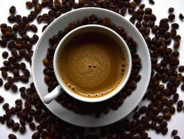 White porcelain cup with coffee and coffee beans on a white background. Tea pair with foamy coffee and coffee beans. photo