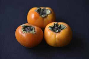 Orange persimmon fruits on a black background. Ripe and juicy persimmon fruits close-up. photo