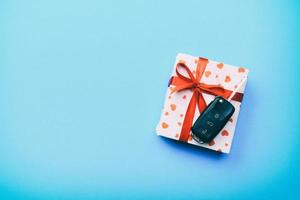 Car key on paper gift box with red ribbon bow and heart on blue table background. Holidays present top view concept photo