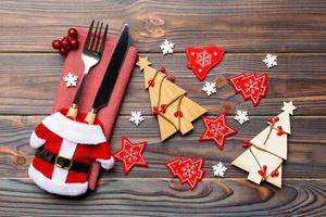 Top view of fork and knife tied up with ribbon on napkin on wooden background. Close up of christmas decorations and New Year tree. Happy holiday concept photo