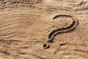 signos de interrogación escritos en la arena de la playa de cerca, con espacio de copia foto