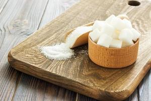 Tazón y cuchara con arena blanca y terrones de azúcar sobre fondo de madera foto