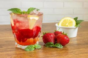 Glass of cold tea with mint,strawberry,lemon, on table photo