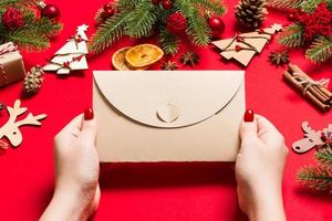 Top view of woman holding an envelope on red background made of holiday decorations. Christmas time concept photo