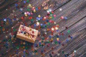 Gift box with star. Creative concept with festive decor on black background. Confetti stars, red, yellow with gift box. Explosion of confetti. Toned photo