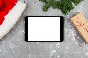 Tablet on Christmas background with santa hat and gift box. New Year holiday photo