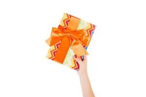 Woman hands give wrapped Christmas or other holiday handmade present in colored paper with orange ribbon. Isolated on white background, top view. thanksgiving Gift box concept photo