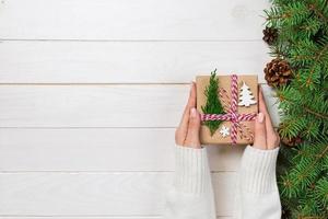 Woman hands give wrapped christmas handmade present in paper with christmas decoration. Present box on holiday on dark wooden table, top view photo