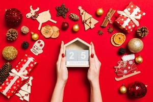 Top view of female hands holding calendar on red background. The twenty fifth of December. Holiday decorations. Christmas time concept photo