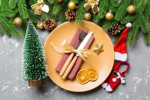 Top view of fork, knife and plate surrounded with fir tree and Christmas decoratoins on cement background. New Year Eve and holiday dinner concept photo