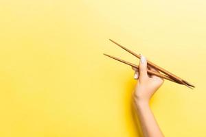 Wooden chopsticks in female hand on yellow background with empty space for your idea. Tasty food concept photo