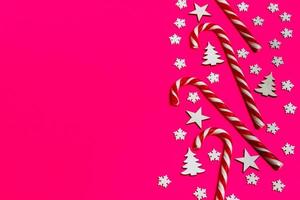 bastón de caramelo de navidad mintió uniformemente en fila sobre fondo rosa con copo de nieve decorativo y estrella. plano y vista superior foto