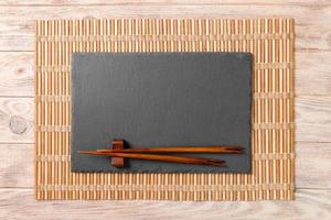 Empty rectangular black slate plate with chopsticks for sushi on wooden background. Top view with copy space photo