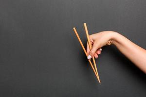 Wooden chopsticks holded with female hands on black background. Ready for eating concepts with empty space photo