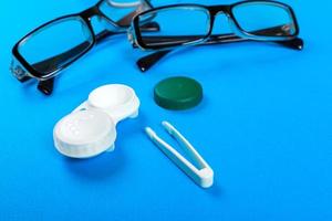 anteojos, lentes de contacto en contenedores y pinzas sobre fondo azul foto