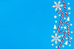 Christmas candy cane lied evenly in row on blue background with decorative snowflake and star. Flat lay and top view photo