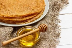 A pile of pancakes, honey, for the celebration of the carnival. Thin pancakes for breakfast. Pancakes and honey Maslenitsa. Pancakes with honey on a white wooden background. space for text photo