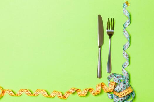 Fork and knife with curled measuring tape on green background with empty space for your design. Top view of proper nutrition concept photo
