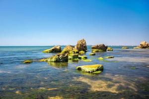 piedra cubierta de algas verdes en el mar con azul cielo como fondo. larga exposición. foto