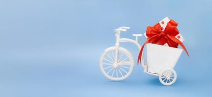 Bicycle with planter box with white box peas red bow on blue background. Holiday, Valentine's, International Women's and Mother's Day, March 8, Birthday. Banner. Copy space photo