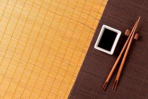 Chopsticks and bowl with soy sauce on two bamboo mat blak and yellow top view with copy space photo