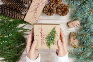 Christmas gift wrapping background. Female hands packaging christmas present wrapped in kraft paper top view. Winter holidays concept flat lay Woman holding Christmas gift box photo