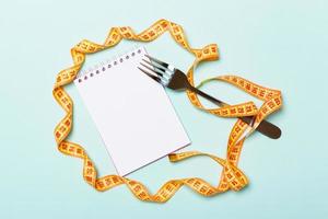 Orange measure tape, open notebook and fork on blue background with empty space for your idea. Top view of healthy lifestyle concept photo