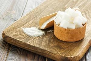 Cuchara de madera y cuenco con azúcar en la mesa, primer plano foto