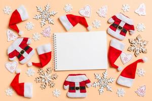 Top view of notebook with Christmas decorations and Santa hats on orange background. Happy holiday concept photo