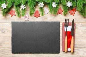 Top view of Christmas dinner on wooden background. Plate, utensil, fir tree and holiday decorations with copy space. New Year time concept photo