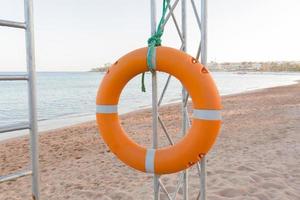 Orange lifebuoy on lifeguard tower on blue sky and beach background photo