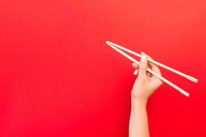 Woman's hand holding chopsticks on red background. Chinese food concept with empty space for your design photo