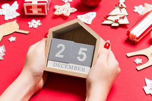 Top view of female hands holding calendar on red background. The twenty fifth of December. Holiday decorations. Christmas time concept photo