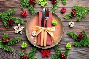 Holiday composition of plate and flatware decorated with Santa hat on wooden background. Top view of Christmas decorations. Festive time concept photo