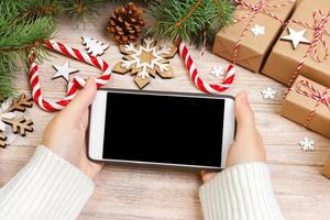 Christmas online shopping. Female buyer makes order at screen of smartphone with copy space. Woman buys presents for xmas eve, sits at home near decorated. Winter holidays sales photo